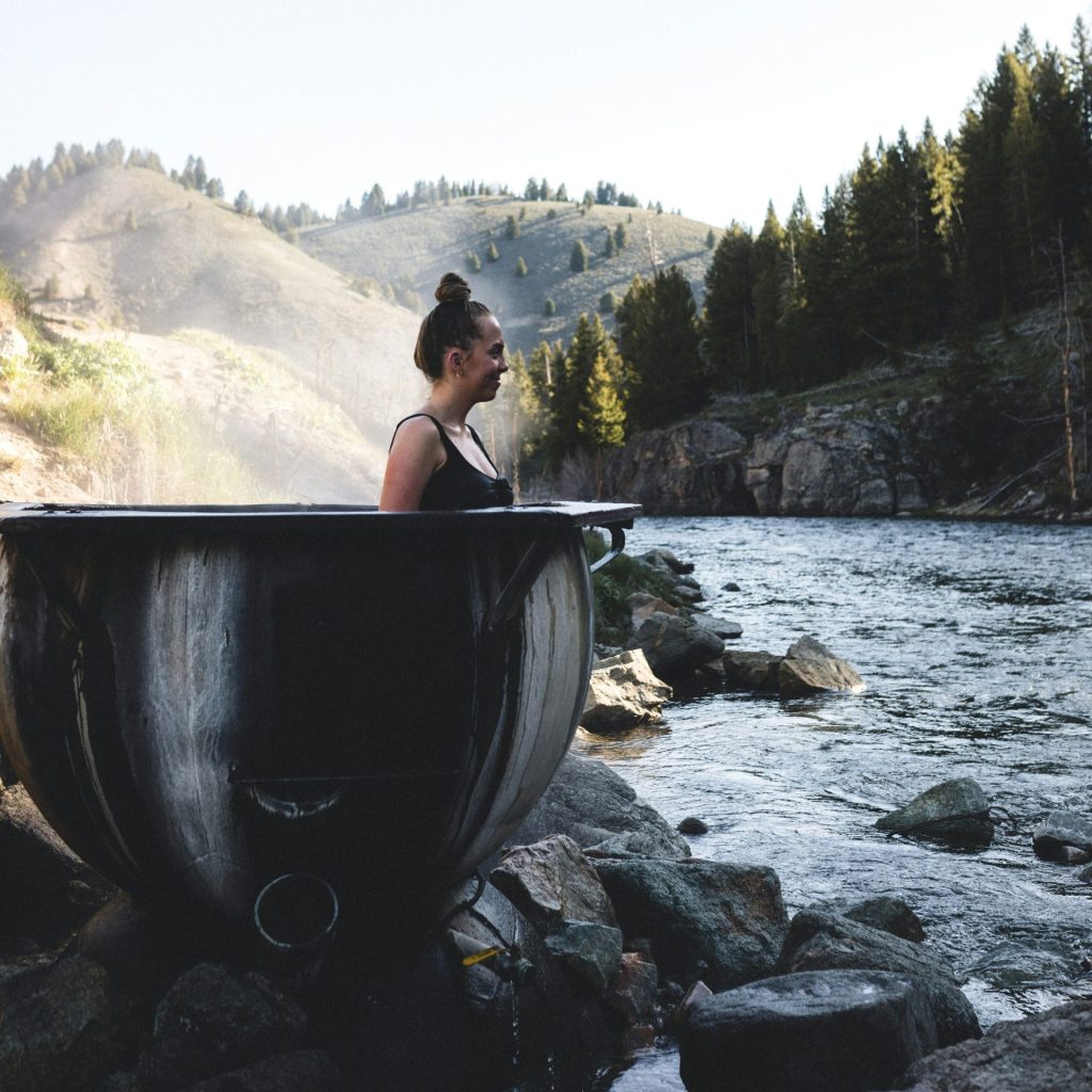 woman in black tank top sitting on gray rock near river during daytime